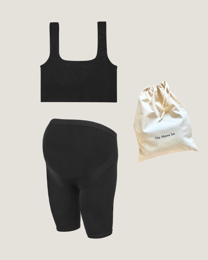 A set of black base layer clothing including a crop top and support shorts, displayed alongside a white drawstring bag.