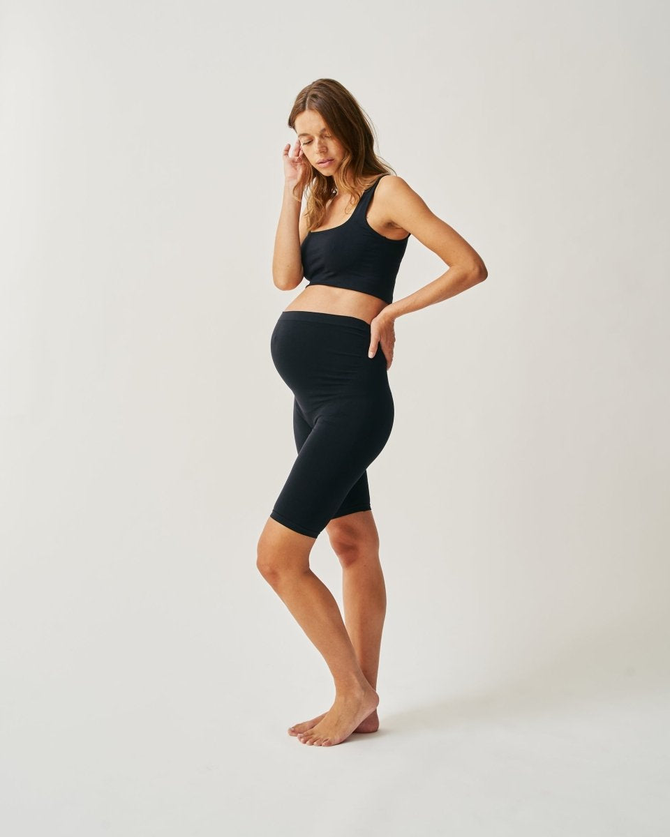A pregnant woman wearing black seamless knit shorts and a matching crop top.