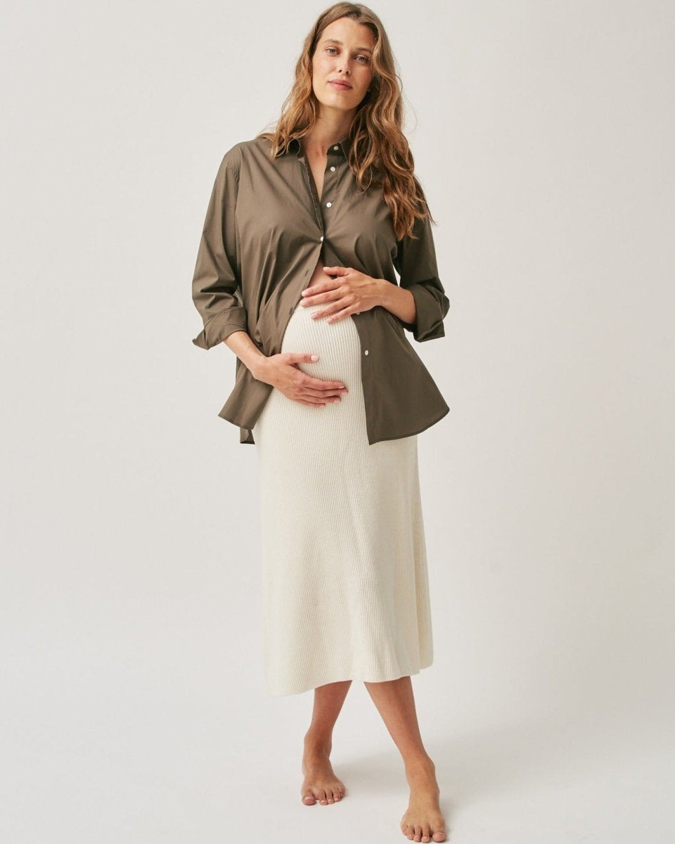 A pregnant woman wearing an oversized olive green poplin shirt paired with a white skirt.