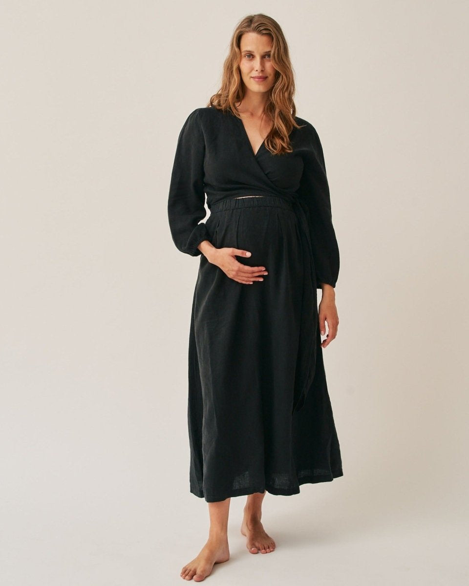 A pregnant woman wearing a black linen wrap dress with long sleeves, standing against a plain background.