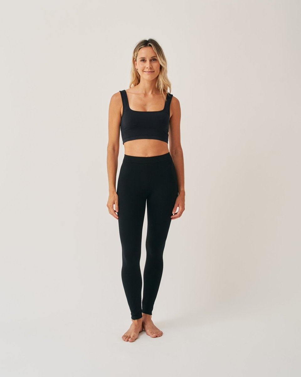 A woman standing in a full-length pose wearing a black high-waist leggings and a matching sports bra.